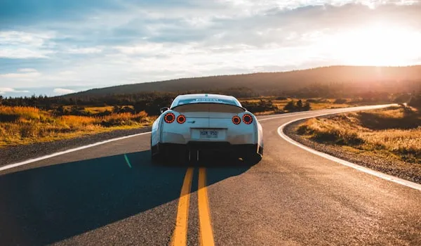 White sports car driving down a rural road at sunset
