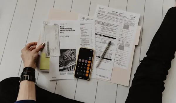 Hand reviewing tax withholding forms next to a calculator and pen