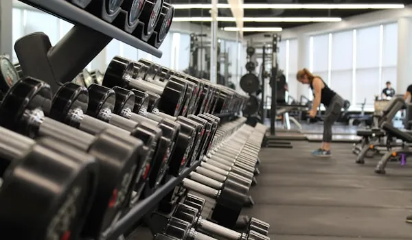 Rack of dumbbells in a gym with a person training in the background